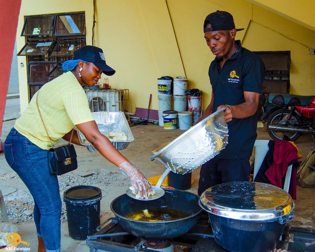 Two members of the KAF Eatables team frying small chops outdoors